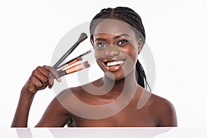 Beautiful african woman with makeup brushes near her face isolated on white background