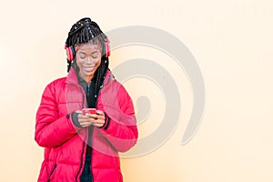 Beautiful African woman outdoors. Black woman listening to music with headphones using smartphone