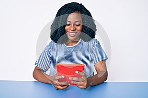 Beautiful african woman using touchpad device looking positive and happy standing and smiling with a confident smile showing teeth