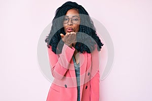 Beautiful african woman wearing business jacket and glasses looking at the camera blowing a kiss with hand on air being lovely and