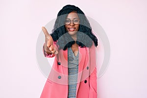 Beautiful african woman wearing business jacket and glasses smiling friendly offering handshake as greeting and welcoming