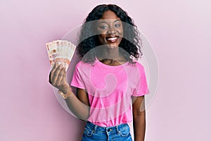 Beautiful african young woman holding 10 colombian pesos banknotes looking positive and happy standing and smiling with a
