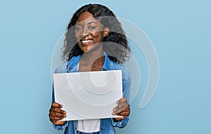 Beautiful african young woman holding blank empty banner looking positive and happy standing and smiling with a confident smile