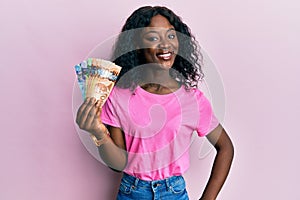 Beautiful african young woman holding canadian dollars looking positive and happy standing and smiling with a confident smile