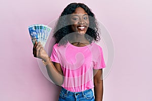 Beautiful african young woman holding south african 100 rand banknotes looking positive and happy standing and smiling with a