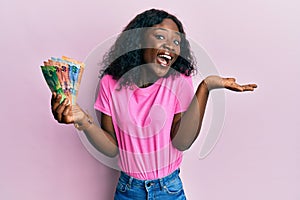 Beautiful african young woman holding south african  rand banknotes celebrating achievement with happy smile and winner expression