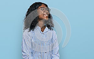 Beautiful african young woman wearing casual clothes and glasses looking away to side with smile on face, natural expression