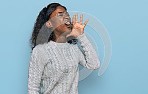 Beautiful african young woman wearing casual winter sweater shouting and screaming loud to side with hand on mouth