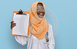Beautiful african young woman wearing doctor stethoscope holding clipboard looking positive and happy standing and smiling with a
