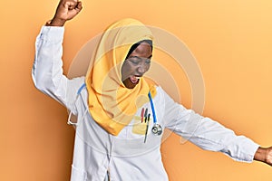 Beautiful african young woman wearing doctor uniform and hijab dancing happy and cheerful, smiling moving casual and confident