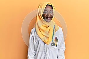 Beautiful african young woman wearing doctor uniform and hijab with a happy and cool smile on face