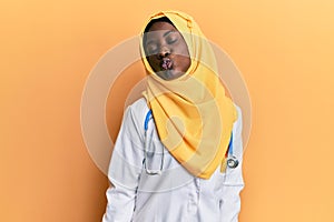 Beautiful african young woman wearing doctor uniform and hijab looking at the camera blowing a kiss on air being lovely and sexy