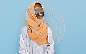 Beautiful african young woman wearing doctor uniform and hijab looking positive and happy standing and smiling with a confident