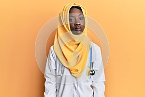 Beautiful african young woman wearing doctor uniform and hijab relaxed with serious expression on face
