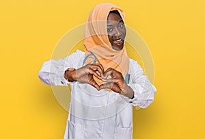 Beautiful african young woman wearing doctor uniform and hijab smiling in love showing heart symbol and shape with hands