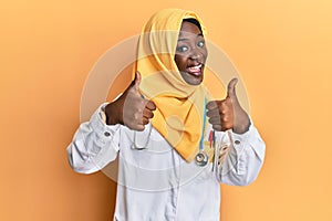 Beautiful african young woman wearing doctor uniform and hijab success sign doing positive gesture with hand, thumbs up smiling