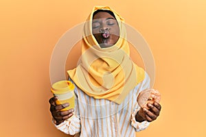 Beautiful african young woman wearing islamic hijab drinking a coffee using smartphone looking at the camera blowing a kiss being