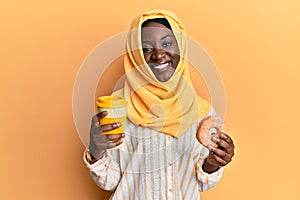 Beautiful african young woman wearing islamic hijab drinking a coffee using smartphone smiling with a happy and cool smile on face