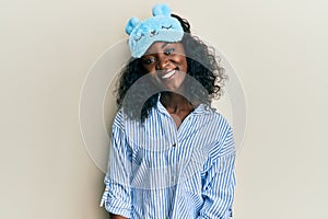 Beautiful african young woman wearing sleep mask and pajama looking positive and happy standing and smiling with a confident smile