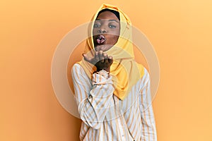 Beautiful african young woman wearing traditional islamic hijab scarf looking at the camera blowing a kiss with hand on air being