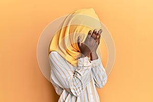 Beautiful african young woman wearing traditional islamic hijab scarf with sad expression covering face with hands while crying