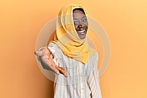 Beautiful african young woman wearing traditional islamic hijab scarf smiling friendly offering handshake as greeting and