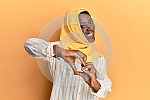 Beautiful african young woman wearing traditional islamic hijab scarf smiling in love doing heart symbol shape with hands