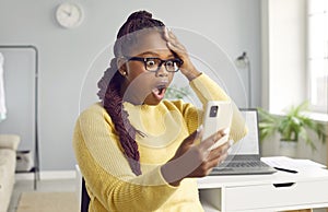 Beautiful africanamerican woman looks at the phone in horror.