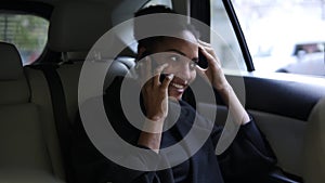 Beautiful Afro American businesswoman sitting on the backseat of a taxi with bright leather salon, talking by her mobile