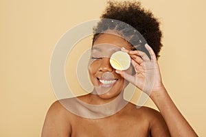 Beautiful afro american female model holding half a lemon in front of her face on a beige background. The concept of