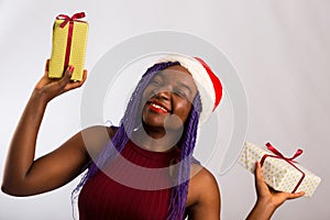 Beautiful Afro American girl in a dress and Santa hat is catching falling presents, looking at camera and smiling, isolated on