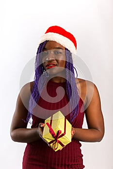 Beautiful Afro American girl in dress and Santa hat is holding presents, looking at camera and smiling, isolated on white