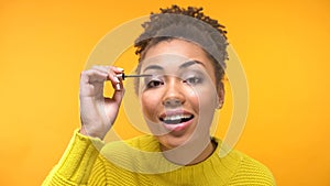 Beautiful Afro-American lady applying eyelash mascara, evening make-up, close up