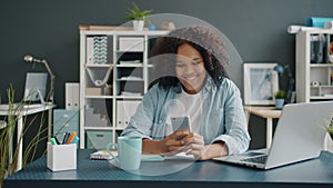 Beautiful Afro-American lady using smartphone touching screen smiling sitting at desk