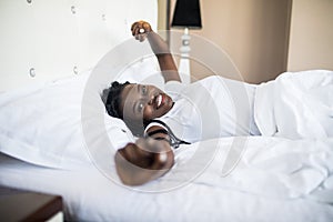 Beautiful afro american woman waking up in her bed, she is smiling and stretching