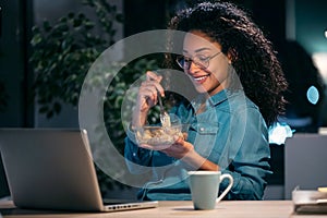 Beautiful afro young business woman working with computer while eating pasta sitting in the office
