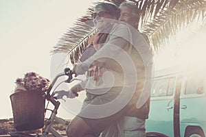 Beautiful aged couple of senior in vacation go both on an old bike and enjoy the summer sunlight. tropical place and vintage van