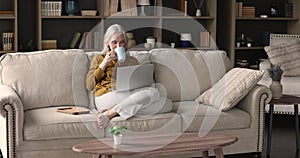 Beautiful aged woman relaxing on sofa with laptop