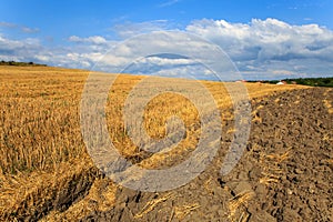 Beautiful landscape with freshly reaped wheat field and ploughed soil against blue sky with clouds photo