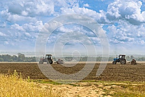 Beautiful agricultural landscape under the cloudy sky - two old tractors equipped with seeders.