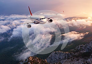 Beautiful airplane is flying over low clouds at sunset