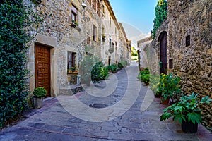 Beautiful alley with old stone houses and pots on the street with plants and flowers, Monells, Girona, Catalonia.