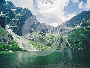 Beautiful alpine lake in the mountains, natural background, summer landscape with blue cloudy sky and reflection in