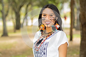Beautiful Amazonian woman with indigenous facial paint and white traditional dress posing happily for camera in park