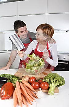 Beautiful American couple working at home kitchen in apron mixing vegetable salad smiling happy