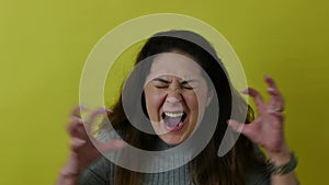 Beautiful angry woman frowning while looking at camera in anger on yellow background.