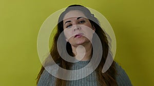 Beautiful angry woman frowning while looking at camera in anger on yellow background.