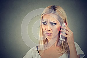 Beautiful angry woman talking on her cell phone on a gray background