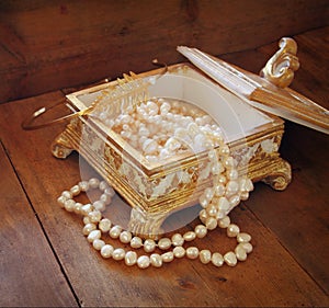 A beautiful antique golden jewelry box with natural white pearls on wooden table. retro filtered image