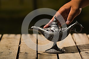 Beautiful antique metal lamp in true Aladin style, hand touching it gently, sitting on wooden surface photo